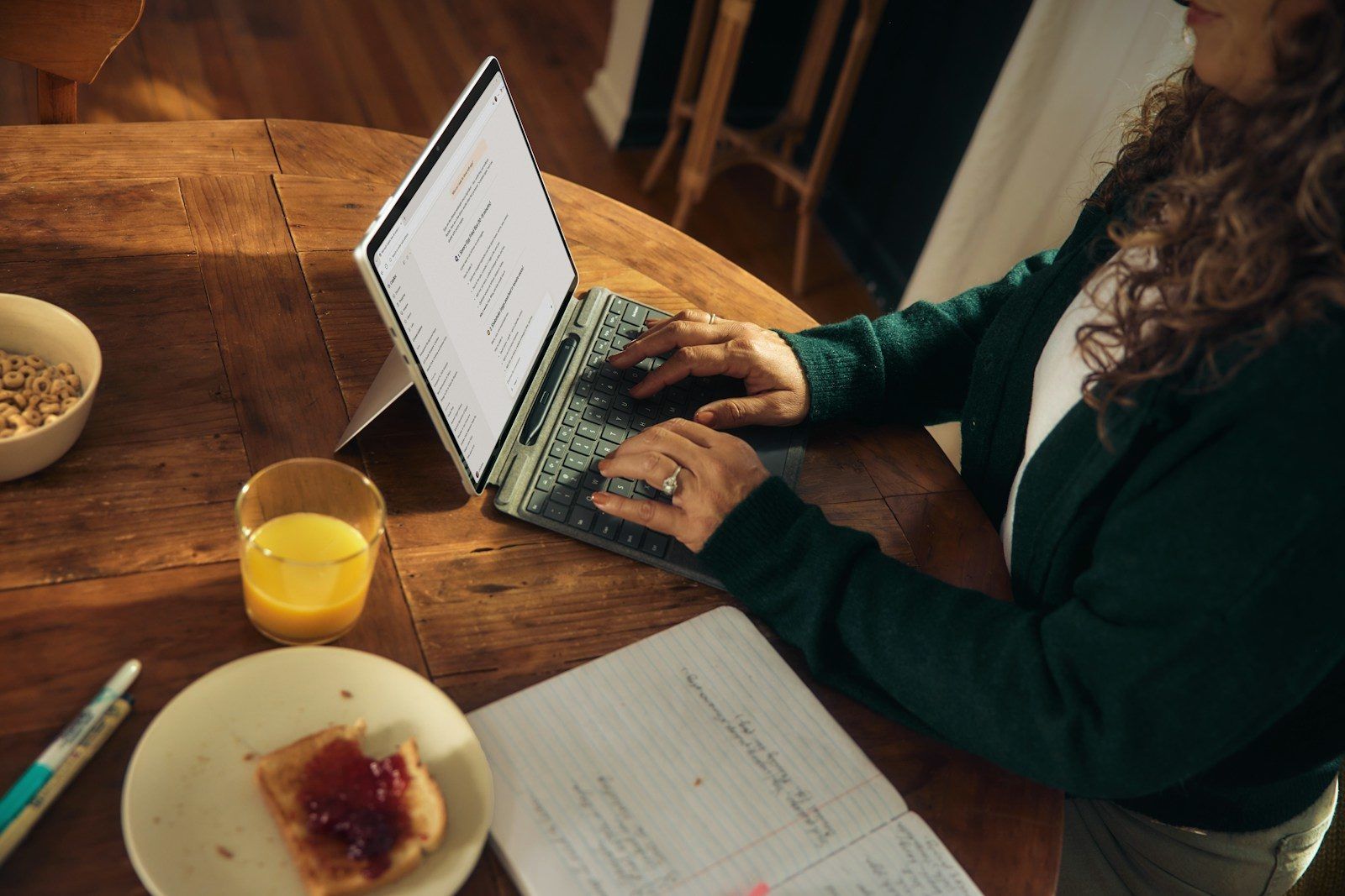 Woman typing on laptop at wooden table with breakfast.